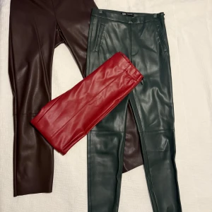 Paketpris: Färgglada skinnbyxor i tre färger - Tre par snygga skinnbyxor i olika färger: ett par mörkbruna/oxröd, ett par mörkgröna och ett par röda. Byxorna har raka ben och klassisk midja, med fickor framtill och dragkedja. Perfekta för dig som vill sticka ut med färg och stil. Paaketpris! Oanvända. (Styck pris: 100 kr)  Färger: Röd, grön och purple/oxbrun/lila  Grön och röd från Zara. Oxbeun/röd från Carin Wester