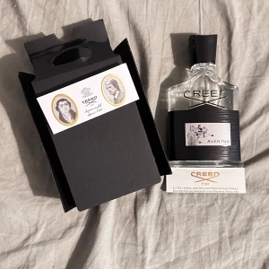 Creed Aventus Eau de Parfum 100ml - Creed Aventus är en exklusiv herrparfym i en elegant genomskinlig glasflaska med svart etikett och silverdetaljer. Kommer i original svart kartong med klassisk Creed-design. Doften är känd för sina fruktiga och träiga noter.