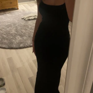 Svart långklänning med smala axelband - Säljer en svart ribbad långklänning med smala axelband och figurnära passform. Klänningen har en enkel och stilren design som passar perfekt till festliga tillfällen. Materialet känns mjukt och följsamt mot kroppen.