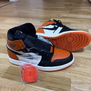 Nike Air Jordans i orange, svart och vitt - Säljer ett par Nike Air Jordans med orange, svart och vit färgkombination. Skorna har klassisk hög siluett, rund tå och snörning. Medföljer extra orange skosnören. Perfekta för dig som vill sticka ut med dina sneakers.