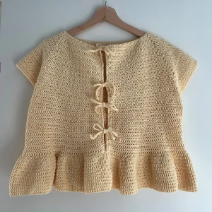 Virkad topp med volang och knytning - Säljer en handvirkad ljusgul topp med korta ärmar, volang nertill och knytband framtill. Toppen är virkad av mig och är ett provexemplar på en kollektion av toppar jag håller på att göra 🌷 Armarna är lite insydda så de blev för stora till en början, men det är inget man tänker på när man har toppen på sig. Jag som bär toppen på bilden har vanligtvis storlek M/L. Säljer toppen lite billigare då det är ett provexemplar 🌟