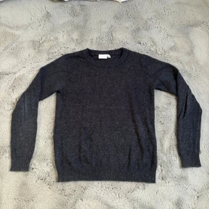 Mörkgrå stickad tröja från Vila - Säljer en enkel och stilren mörkgrå stickad tröja från Vila. Tröjan har rund halsringning och långa ärmar med ribbade muddar vid ärmslut och nederkant. Perfekt för lager-på-lager under kyliga dagar.