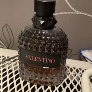 Valentino herrparfym (coral fantasy) - Lyxig herrparfym från Valentino i en mörk, diamantmönstrad glasflaska med svart etikett och stor svart kork. Flaskan har en exklusiv och modern design som sticker ut på hyllan.