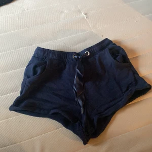 Mörkblå shorts med satin snörning - Mörkblå mini shorts från Iconic Sport med elastisk midja och bred satinliknande snörning framtill. Shortsen har två fickor och är tillverkade i mjuk bomull Ena snöret har plasten gått upp
