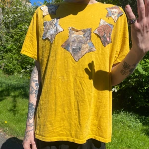 Gul t-shirt med hundmotiv - Gul t-shirt med unika tryck av olika hundar framtill. Köpt second hand och stjärnorna sitter löst på vissa ställen från t-shirten vilket kan eller inte behöver vara så den är tänkt. I vilket fall som helst så tillför det som nice detalj till tröjan :-P