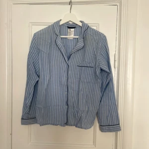 Blåvit randig pyjamasskjorta från H&M - Säljer en blåvit pyjamasskjorta från H&M i storlek XS. Skjortan har lång ärm, klassisk krage och knäppning framtill. Detaljer med mörkare kant vid bröstficka och ärmslut. 