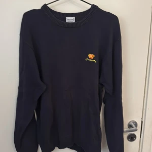 Mörkblå stickad tröja från Trimingham's ovanlig tröja - Säljer en mörkblå stickad tröja från Trimingham's Bermuda i 100% bomull. Tröjan har rund halsringning och ett broderat emblem med krona och texten 'Bermuda' på bröstet. Perfekt för dig som gillar klassisk stil. Ovanlig 