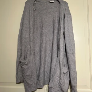 Grå kofta från Vila - Mysig och enkel grå kofta från Vila i storlek XL. Koftan har långa ärmar, två fickor framtill och är tillverkad i ett mjukt stickat material. Perfekt att slänga på sig när det är lite kyligt ute.