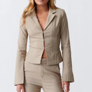 Beige kavaj från Gina Tricot - Säljer en beige kavaj från Gina Tricot med klassisk krage och figurnära passform. Jackan har långa ärmar och stängs med diskreta knappar framtill. Perfekt för en stilren och trendig look.