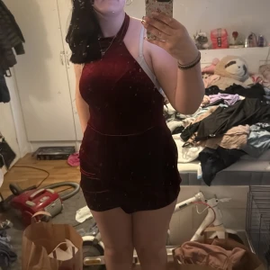 Vinröd sammetsklänning med halterneck - Säljer en vinröd sammetsklänning med halterneck och öppen rygg. Klänningen är kort och har en tight passform som framhäver figuren. Perfekt för dig som vill sticka ut med en elegant och trendig look.