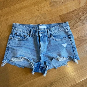 Ljusblå jeansshorts med fransar från Pull&Bear - Säljer ett par ljusblå jeansshorts från Pull&Bear med råa fransade kanter och slitningar framtill. Klassisk femficksmodell med bälteshällor och knappgylf. Perfekta för sommaren!