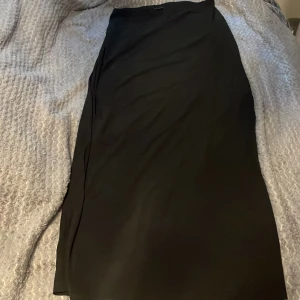 Svart långkjol från Gina Tricot - Säljer en svart långkjol från Gina Tricot. Kjolen har en enkel och stilren design med rak passform och är perfekt för dig som gillar minimalistisk stil. Lätt att matcha med olika toppar och skor.