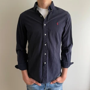 Mörkblå skjorta från Ralph Lauren - Säljer en klassisk marin blå skjorta från Ralph lauren. Skjortan har en broderad logga på bröstet och passar perfekt inför sommaren☀️✅ skjortan är endast använd ett fåtal gånger och är i super fint skick🤩det är bara att skriva om du har några funderingar🔝 nypris:1200kr mitt pris449kr priset är aldrig hugget i sten🪨