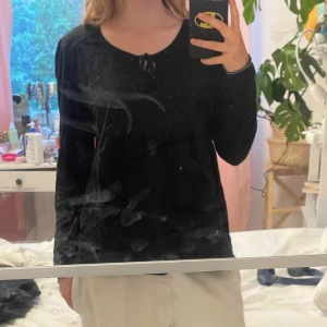 Svart långärmad topp med knyt - Säljer en svart långärmad topp med knyt vid halsringningen. Toppen har en mjuk och bekväm passform och är perfekt för en enkel men stilren look. Ca storlek M/L