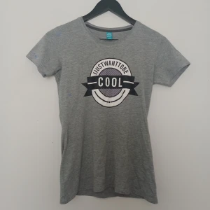 Grå t-shirt med IJWTBC logo - Grå t-shirt med IJustWantToBeCool logo. Har lite blå målarfärg och ett litet håll. Klassisk rund halsringning och korta ärmar. Perfekt för dig som gillar IJWTBC 