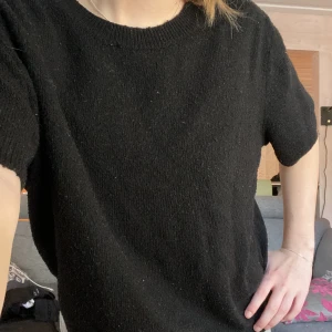 Svart stickad tröja från H&M - En svart stickad tröja från H&M med korta ärmar och rund halsringning. Tröjan har en avslappnad passform och är perfekt för lager-på-lager-stil. Enkel och stilren design som passar till många outfits. Den har tydliga tecken på användning då den är nopprig.