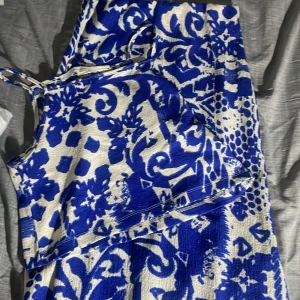 Blåvit mönstrad kjol och topp  från Atmosphere - Säljer en blåvit kjol och topp från Atmosphere med ett iögonfallande abstrakt mönster. Kjolen och toppen har smala axelband och är ärmlös, perfekt för varma dagar. Materialet är lätt och har en struktur som ger extra karaktär. Storleken är m men är som ett s