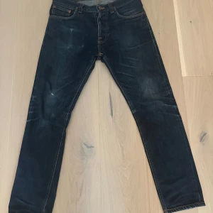 Mörkblå jeans från Nudie  - Säljer ett par mörkblå jeans från Nudie Jeans med klassiska orange sömmar och en button fly. Modellen är fearless Freddie. Hör av er om ni har frågor!