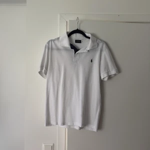 Ralph Lauren Pikétröja  - Klassisk vit pikétröja från Ralph Lauren med korta ärmar och broderad logga på bröstet. Perfekt till sommaren och enkel att matcha med det mesta. Snygg krage och normal passform. Tröjan är i perfekt skick och det finns inga skador. Den är i storlek M. Om det finns frågor är det bara att höra av sig👍