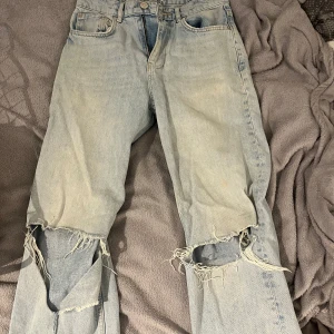 Ljusblå jeansbyxor från Gina - Ljusblå jeansbyxor från Gina Tricot med klassisk femficksdesign och dragkedja. Byxorna har stora slitningar och hål vid knäna för en riktigt edgy look. Perfekta för dig som gillar en avslappnad och trendig stil.