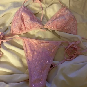 Rosa bikini med paljetter och knyt - Säljer en ljusrosa bikini med glittrande paljetter. Både överdelen och underdelen har knytband för justerbar passform. Perfekt för dig som vill sticka ut på stranden!