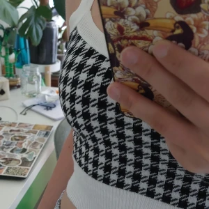 Svartvit mönstrad topp - Säljer ett croppat linne med svartvitt hundtandsmönster. Toppen har breda axelband och ribbad nederkant samt kant i vitt. Perfekt för sommaren och enkel att styla till olika outfits.