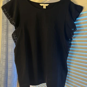 Svart blus med volangärmar från H&M - Svart blus från H&M med korta volangärmar i spets. Rund halsringning och rak passform. Perfekt för dig som vill ha en enkel men ändå detaljrik topp.