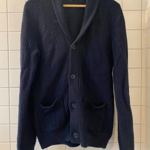 Mörkblå stickad kofta från Dressmann - Säljer en mörkblå stickad kofta från Dressmann i storlek S. Koftan har långa ärmar, knäppning framtill med fyra knappar och två fickor. Perfekt för lager-på-lager och passar till många tillfällen.