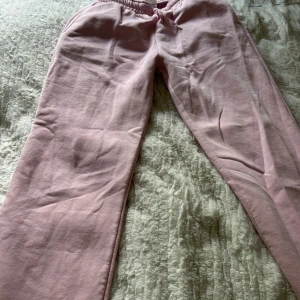 Ljusrosa mjukisbyxor från Gina Tricot - Ljusrosa mjukisbyxor från Gina Tricot med resår och dragsko i midjan. Byxorna har en avslappnad passform och är tillverkade i mjuk bomull, perfekta för en chill vardagslook.