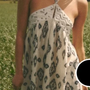 Vit och svart mönstrad halterneckklänning - Säljer en vit kortklänning med svart grafiskt mönster och halterneck. Klänningen har dekorativa detaljer upptill och en lös passform som ger en luftig känsla. Perfekt för varma dagar och enkel att styla med sandaler eller sneakers.