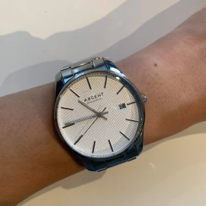 Silverfärgad klocka från Axcent - Stilren klocka från Axcent med silverfärgat armband i metall och rund urtavla. Har datumvisning. Några små repor, exempelvis ovanför texten där det står ”Axcent”. Batteri behöver bytas. Jag sätter ett lågt pris då jag förstår det är svårt att veta om den passar, men jag skulle säga att jag har en smal handled.
