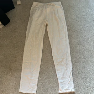 Vita linnebyxor med dragsko - Säljer ett par vita linnebyxor med elastisk midja och dragsko. Byxorna har raka ben och en bakficka. Perfekta för varma dagar och ger en avslappnad look.
