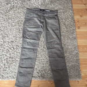 Grå jeansbyxor från Replay Anbass - Säljer ett par grå jeansbyxor från Replay, modell Anbass. Klassisk femficksdesign med snygga sömdetaljer på bakfickorna och normal passform. Perfekta för dig som gillar stilrena och bekväma jeans. Bra skick och sällan använt