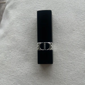 Rouge Dior läppstift 453 Adoré - Säljer ett lyxigt Rouge Dior läppstift i nyansen 453 Adoré. Hylsan är svart med silverdetaljer och har den klassiska CD-loggan. Läppstiftet har en elegant rödrosa färg och ger en snygg finish till läpparna.  Kommer utan förpackning, oanvänd och otestad, om du köper fler av dessa läppstift kan jag tänka mig bättre pris. Rensning inför flytt. Vissa märken på själva skalet på läppstiftet kan förekomma då jag förvarat alla i samma låda 