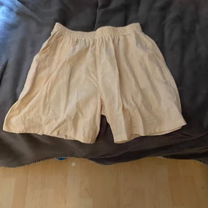 Beiga loose linneshorts med resår - Säljer ett par beiga shorts i loose fit med resår i midjan. De är tillverkade i svalt linne och har en enkel, stilren look som passar perfekt till varma dagar. Luftiga och bekväma med avslappnad känsla.