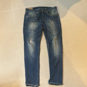 Dondup jeans  - Snygga blå jeans från Dondup med coola slitningar och lagade hål med röd detalj. Klassisk femficksmodell, kontrastsömmar och normal passform. Tillverkade i Italien i mjukt jeanstyg. Perfekta för en avslappnad streetstil. Modellen är George, finns fler jeans på profilen 