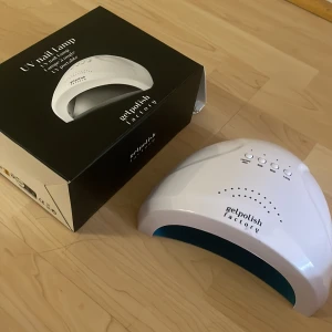 UV-nagellampa Gelpolish Factory - UV-nagellampa från Gelpolish Factory i vit plast med digital timer och flera inställningar. Perfekt för att härda gelnagellack hemma. Kommer med originalkartong och har en snygg, modern design.