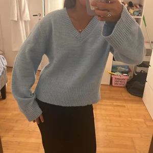 Ljusblå stickad v-ringad tröja - Supermysig ljusblå stickad tröja med v-ringning och breda ribbade muddar vid ärmslut och nederkant. Tröjan har en loose passform och långa ärmar, perfekt för lager på lager. Enkel att styla med både jeans och kjol. Storlek 158/164 (xxs) från Gina Young💞