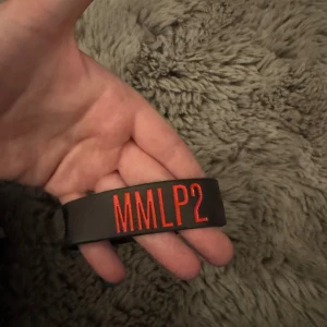 Svart MMLP2 armband Eminem - Coolt svart armband med texten MMLP2 i rött och präglad Eminem-logga. Perfekt för dig som älskar Eminem och vill visa det med stil. Tillverkat i mjukt syntetmaterial som är bekvämt att bära hela dagen.