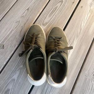 Olivgröna sneakers från Axel Arigato - Snygga olivgröna sneakers från Axel Arigato med vit sula och häl. Skorna har klassisk snörning och är tillverkade i canvasmaterial. Storlek 38 men jag som har storlek 36/37 har kunnat ha dom utan problem!! 