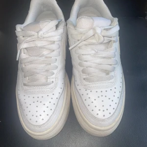 Vita Nike Air  - Klassiska vita Nike Air sneakers i skinn med perforerad tå, rund tå och platt hög sula. Snygg och tidlös modell med snörning och diskret Nike-logga på sidan. Perfekta för en clean och sportig look. Rengörs innan leverans. Fint skick annars!!