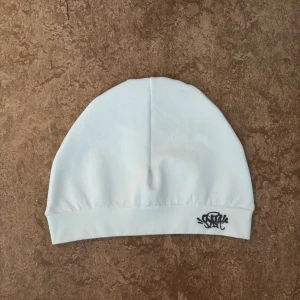 Syna World Skull Cap – Vit - Syna World Skull Cap i vit – helt ny och oanvänd! Tillverkad i mjuk bomull för en skön känsla. Enkel och clean design som passar till streetwear och vardagsstil. Den rena vita färgen lyfter vilken outfit som helst och gör den till ett måste för dig som vill sticka ut med stil. Kommer i originalförpackning med tillhörande taggar och nyckelring.
