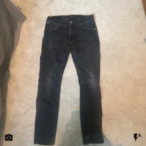 Nudie Jeans - Snygga svarta jeans från Nudie Jeans W30 L30  med slim fit. Jeansen har mörk tvätt, diskreta slitningar och Nudie-logga på bakfickan. Perfekt för everyday-use. S