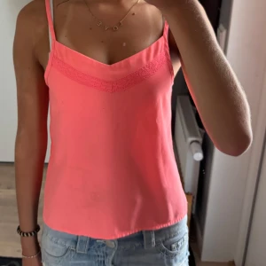 Rosa linnetopp med spetsdetalj - Snygg rosa linnetopp med smala, justerbara axelband och spetsdetalj längs v-ringningen💕Den har en fläck som inge gör bort i tvätten, därför säljer jag den billigt, fläcken synd däremot mest på väldigt nära håll💕 Lappen med storlek är bortklippt men skulle gissa på xxs med tanke på hur den sitter på mig💕