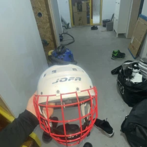 Hockey Vit Jofa hjälm med rött galler  - Säljer en klassisk vit Jofa hjälm med rött galler, perfekt för hockey eller bandy. Hjälmen har vadderad insida för extra komfort och justerbart hakband. Snygg och sportig look med tydlig Jofa-logga på sidan.
