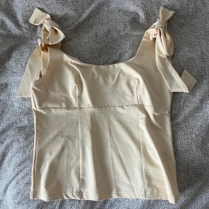 Beige linnetopp med knytband - Supersöt beige linnetopp med breda axelband som knyts i stora rosetter på axlarna. Toppen har en rak passform och är tillverkad i mjukt bomullstyg. inte använt någon gång , ser ut exakt som den från zara 💛