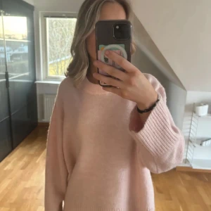 Ljusrosa stickad oversized tröja - Supermysig ljusrosa stickad tröja med oversized passform och långa ärmar. Perfekt för kyliga dagar och enkel att styla med jeans eller kjol. Tröjan har en rund halsringning och breda ribbade muddar vid ärmsluten.
