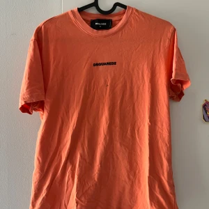 Orange t-shirt från Dsquared2 - Snygg orange t-shirt från Dsquared2 med svart logga tryckt på bröstet. Klassisk rund halsringning och korta ärmar. Tillverkad i mjuk bomull som känns skön mot huden. Perfekt för dig som gillar streetwear och vill sticka ut med färg. Mindre fläck! 