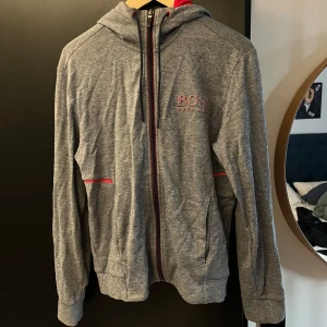 Hugo Boss hoodie grå röd - Unik och stilren hoodie från Hugo Boss. Den är grå med röda detaljer som är reflektiva (se bild 3) . Den är bra skick och knappt använd. Storleken är S. Hör av om ni har frågor och funderingar.