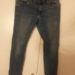 Blå smala jeans från Lindex - Snygga blå jeans från Lindex i smal passform. Klassisk femficksmodell med normalhög midja och lätt slitningar för en cool look. Jeansen är gjorda i mjukt denimtyg och passar perfekt till vardagsstilen.